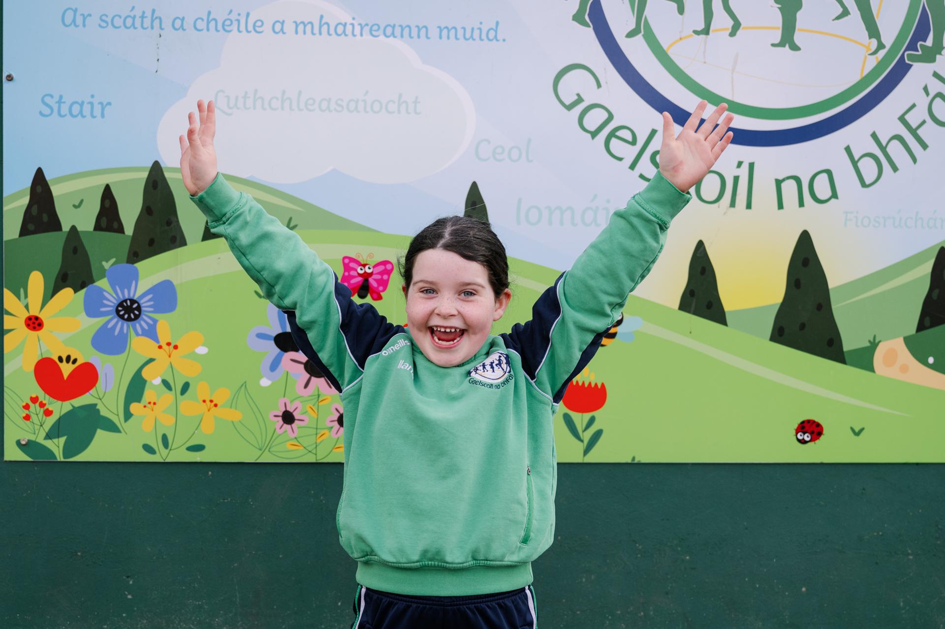 Páiste sona taobh amuigh lena lámha san aer ag súgradh / Happy child outside with hands in the air playing